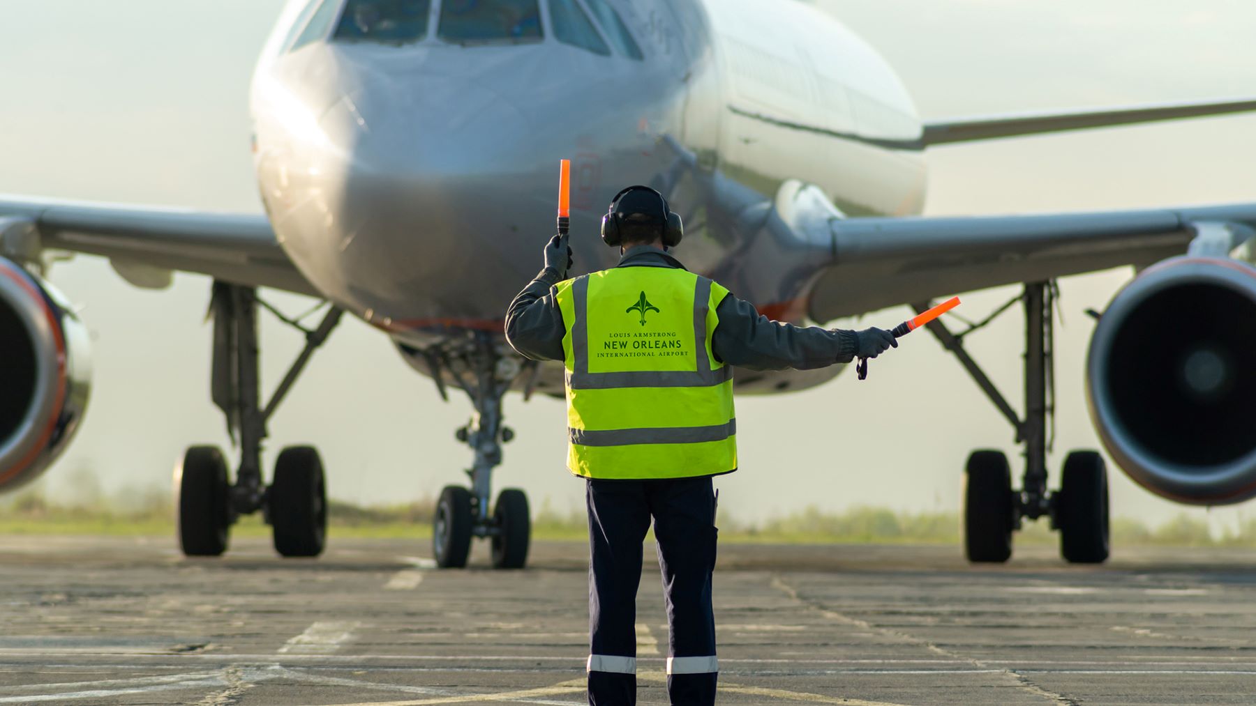 New Orleans Airport employee wearing branded vest, directing an airplane